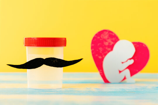 Test-tube of sperm with felt moustache and heart with embryo. Yellow background. Concept of artificial insemination