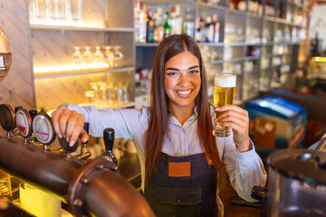 Beautiful smiling female Bartender serving a draft beer at the bar counter , shelves full of...