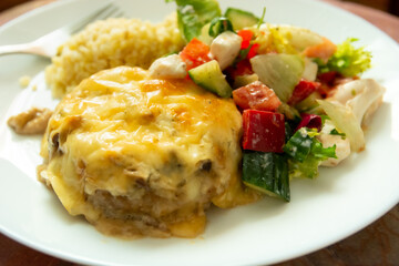 Dinner dish with large minced cutlet with yellow cheese and salad with peppers, cucumber and white...