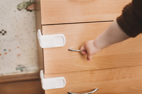 A small child opens a chest of drawers wardrobe with child protection. Dangerous situation at home. Child opening dresser drawer