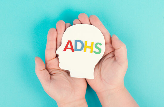Hands holding a head with the german word ADHS which means attention deficit hyperactivity disorder, ADHD symptom, mental health
