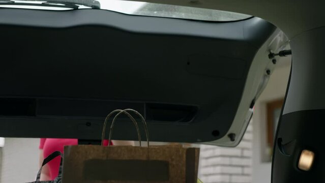 Woman Picks Up Shopping Bags From The Trunk Of A Car. Girl Takes Packages From The Car At Home.