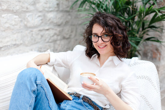 Happy girl reading book and drinking coffee at home. Young woman