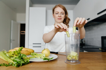 Woman preparing green smoothie in her kitchen