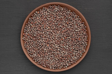 Mustard seeds in clay plate on black wooden background. Macro. Vegetarian food concept