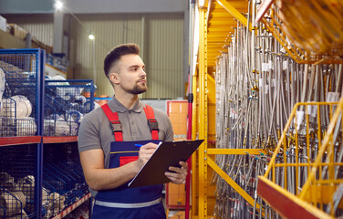 Young man who works as a salesman or manager at a modern DIY store or shopping mall taking notes on his clipboard while checking stainless steel hoses in one of the hardware aisles