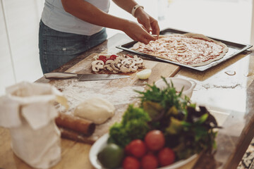 Obraz na płótnie Canvas A woman prepares homemade pizza with vegetables and mushrooms in the kitchen. Pizza cooking process