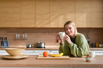 Young woman drinking coffee or tea at home in the kitchen