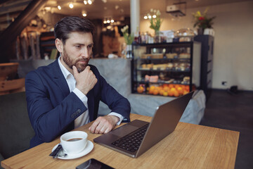 Handsome Caucasian thoughtful serious businessman sitting at laptop and thinking in cafe. Portrait.