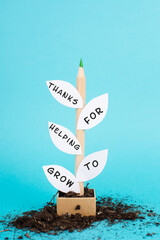 Plant made from a pencil and paper, the phrase thanks for helping to grow is standing on the...