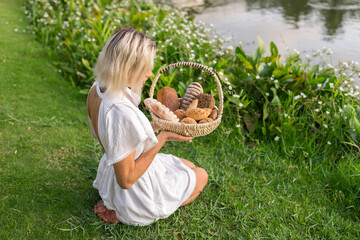 Young woman in white dress sitting on the grass with basket with assorti of brown and white homemade bread. High quality photo