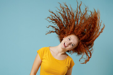 Young smiling happy redhead woman 20s wearing yellow t-shirt dance waving fooling around have fun enjoy play fluttering hair isolated on plain light pastel blue background. People lifestyle concept.