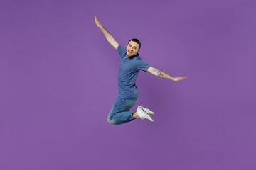 Full body young cheerful fun cool man 20s wear basic blue t-shirt jump high with outstretched arms hands like flying isolated on plain purple color background studio portrait People lifestyle concept