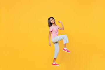 Fototapeta na wymiar Full body little kid girl of African American ethnicity 12-13 years old in pink t-shirt doing winner gesture celebrate raise up leg isolated on plain yellow background. Childhood lifestyle concept