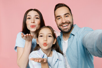 Close up young happy lovely parents mom dad with child kid daughter teen girl in blue clothes doing selfie shot pov on mobile cell phone blow air kiss isolated on plain pastel light pink background