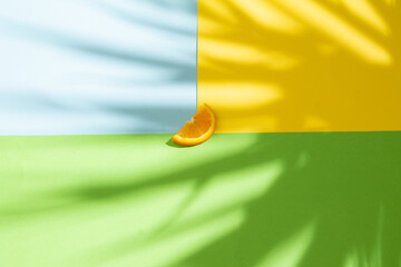 Orange slice with palm tree shadow on yellow, blue, green background. Summer vacation concept.