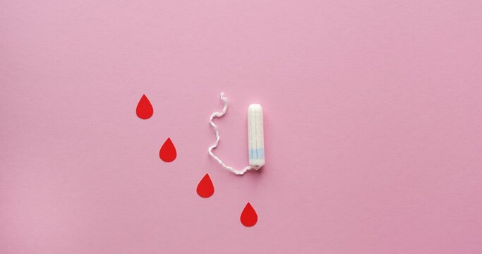 Women's tampon and drops of blood cut out of paper in a shape of heart. Menstrual cycle. Looped 4K stop motion animation on pink background