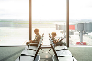 Children play games on tablet or smartphone, while waiting for their airplane flight in transit...