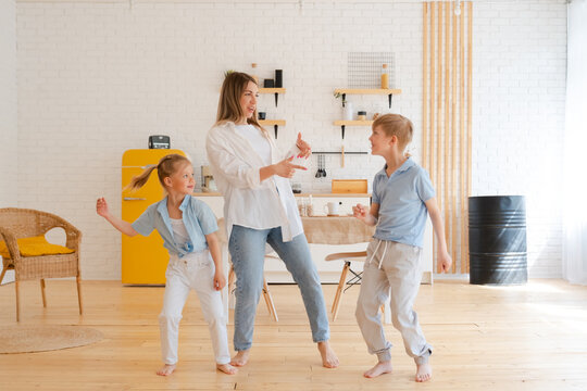 Happy emotional dance of mother with her two children, active modern family enjoy activities at home in living room. Motherhood and childhood, listening to music together, having fun