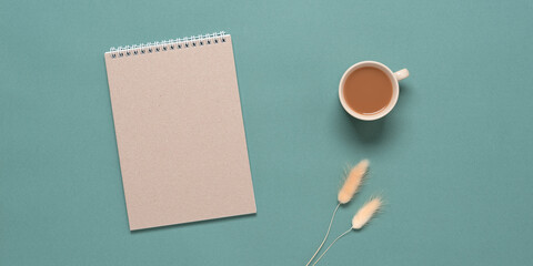 Brown craft notepad, cup of coffee and dried lagurus grass. Home office desk. Turquoise pastel background. Top view, flat lay. Banner
