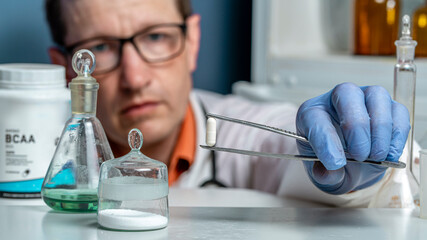 Sport Nutrition Supplement in lab. The doctor is holding a BCAA capsule in tweezers.