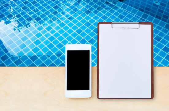 Smartphone with blank paper sheet on wooden clipboard over clean swimming pool water