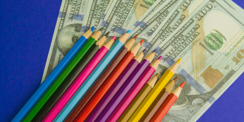 multicolored pencils on souvenir dollar bills. items lie on a blue background. Banner for insertion...
