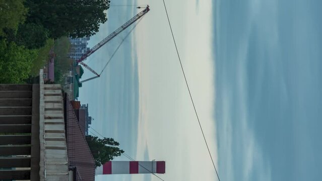 Close-up of the TPP pipe next to the crane. Rain clouds in the background. Trees and unfinished concrete building swaying in the foreground. Timelapse. Vertical video