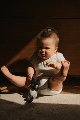 A 7-month girl is stretching her legs on the carpet dressed in a bodysuit