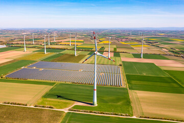 Panorama of solar panels of a solar park amidst wind turbines between agricultural fields