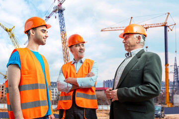 Older construction supervisor with younger worker helper at construction site. Managers wearing...