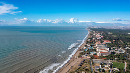 Fototapeta premium Drone view of the sea coast in Belek, Antalya, Turkey. Mountains with snow caps, clouds and sunlight over the sea. Aerial footage over the Mediterranean coast