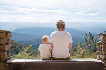 Fototapeta premium rear view father and son sitting together outdoors on the bench and enjoying beautiful nature view