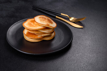 Delicious fresh pancakes on a black plate against a dark concrete background