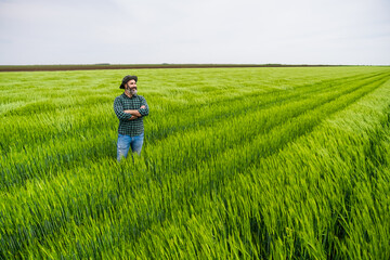 Naklejka na ściany i meble Happy farmer is standing in his growing wheat field.