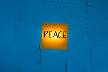 back lit yellow office note card paper with peace written on blue  background