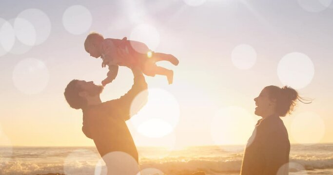 Animation of bokeh over happy caucasian family playing on beach at sunset