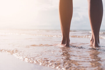 Close up woman legs walking on tropical sunset beach with smooth wave and bokeh sun light wave abstract background. Travel vacation and freedom feel good concept. - obrazy, fototapety, plakaty