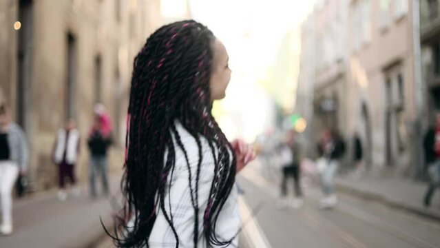 Portrait of attractive young woman with flying hair walking down the street and turn around. Close up view of happy girl with dreadlocks. 