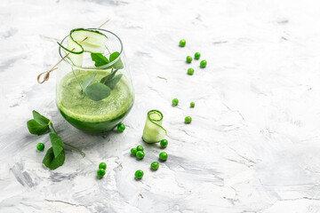 cucumber green smoothie in a glass on light concrete background. Detox smoothie, green fresh peas, cucumber, spinach and lime. top view
