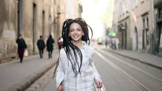 Portrait of attractive young woman with flying hair walking down the street and turn around. Close up view of happy girl with dreadlocks. 