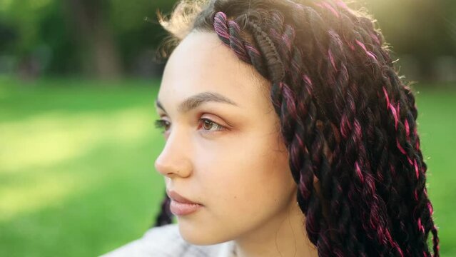 Portrait of attractive dark haired woman with dreadlocks while standing in the sunny city street. Beautiful woman looking ahead outside.