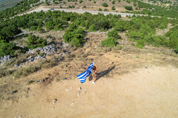 Happy tourist traveler girl with huge flag of Greece standing on the top of the mountain. Freedom, hope, peace concept