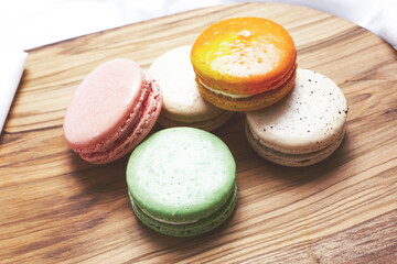 A view of a pile of colorful macaron cookies on a wood board.