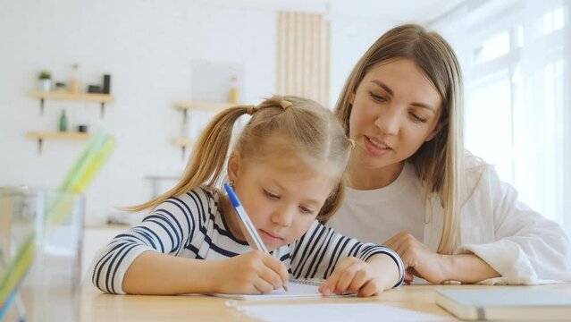 Mother and little 6 year old daughter study writing letters at home, mom helps her preschool girl to do homework to prepare for school classes. Support and motivation, parent and child