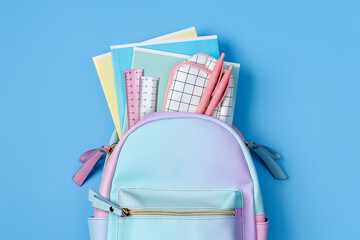 Opened School backpack with stationery in pastel color on blue background. Concept back to school....