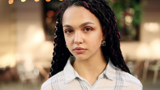 Portrait of attractive dark haired woman with dreadlocks while standing in the city street. Beautiful woman looking at the camera outside.