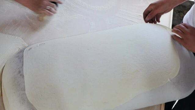 view from above two women bakers make thin dough by rolling out with a rolling pin and put on a jigging pad for baking Armenian pita in tandoor. slow motion