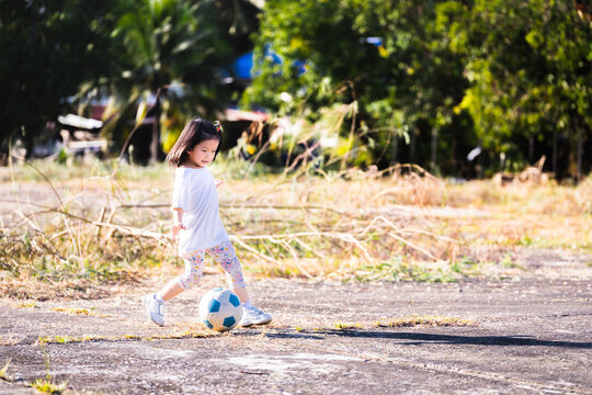 Portrait image active girl 5 years old. Child playing football in summer time. Happy kid running with funny. Children exercise on cement field. Empty space for entering text. Asian baby practicing.