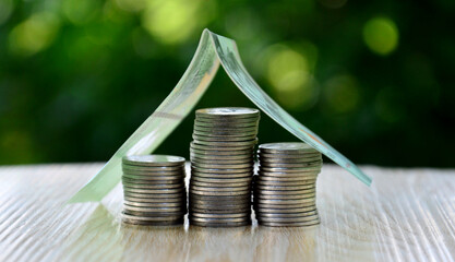Stacked coins grow with banknotes on the roof. Financial growth concept.